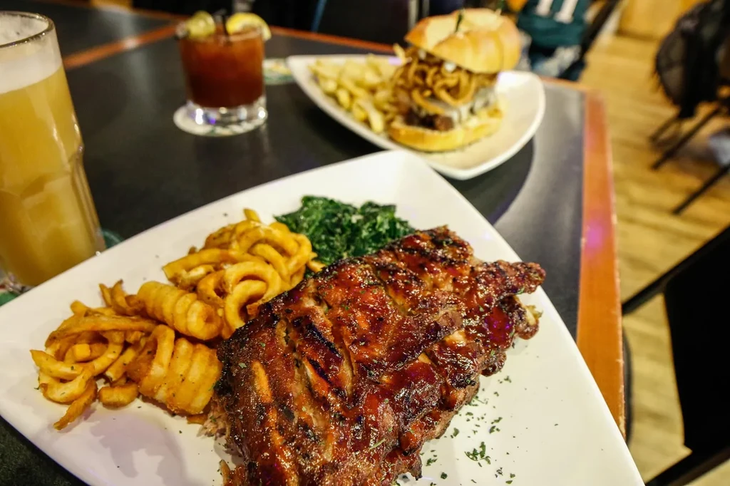 BBQ ribs, curly fries, greens, and beer on a restaurant table.