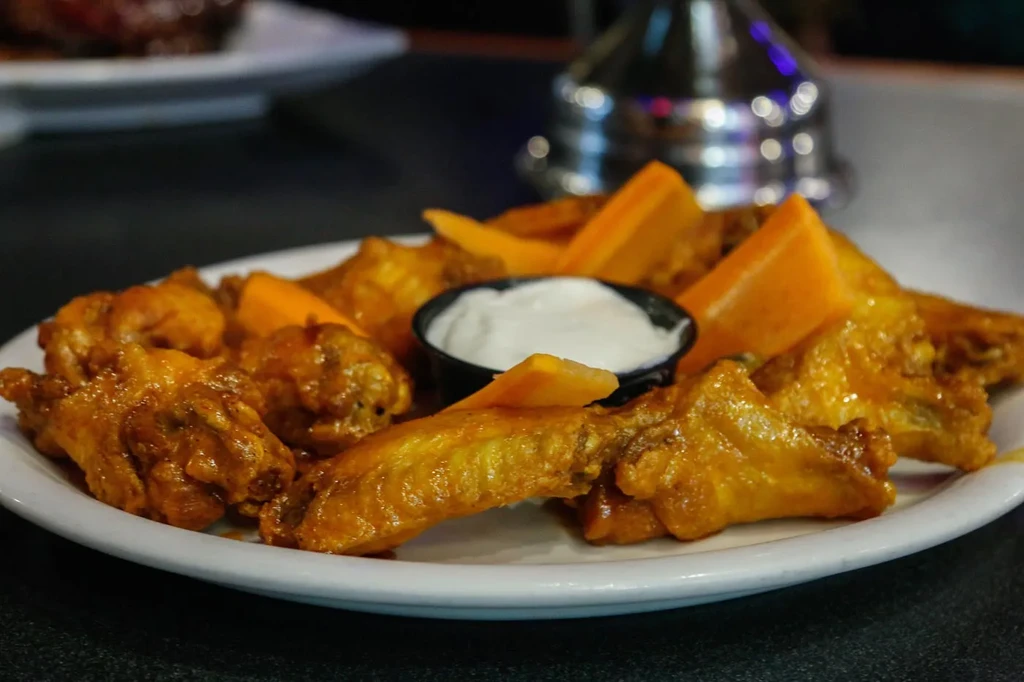 Plate of saucy chicken wings, cheddar cheese wedges, and dipping sauce.