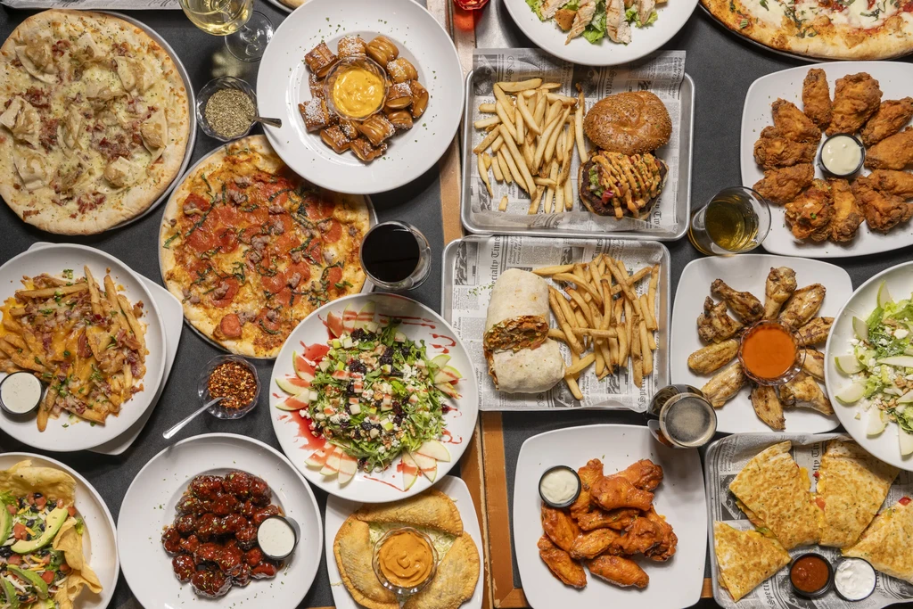 Overhead shot: large variety of food and drinks on a dark table.