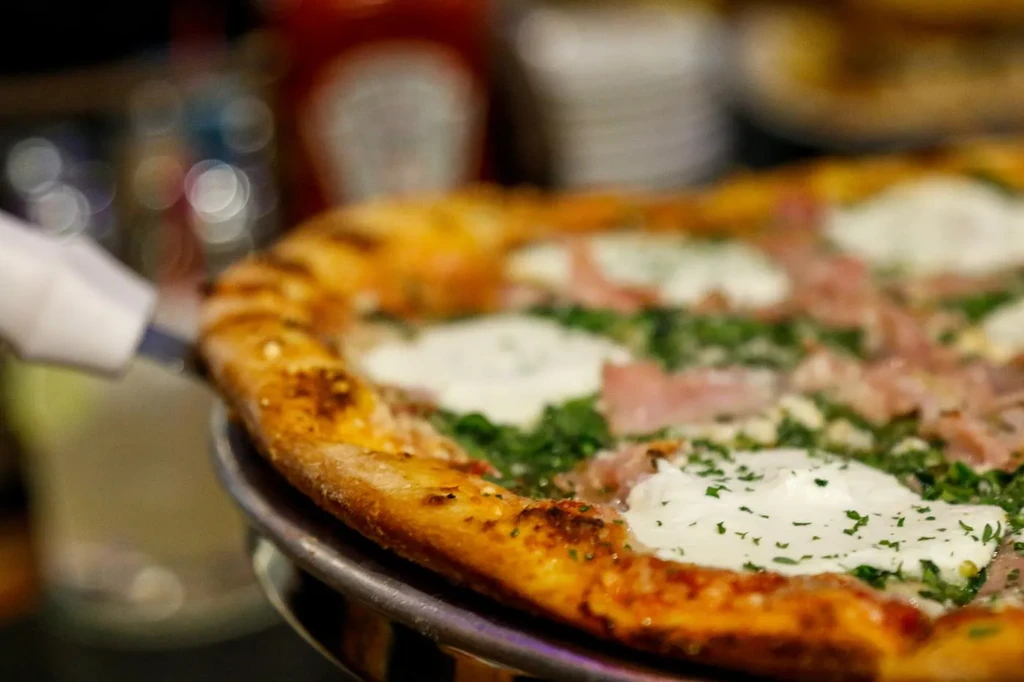 Pizza close-up: golden crust, char marks, herbs, white cheese, prosciutto.