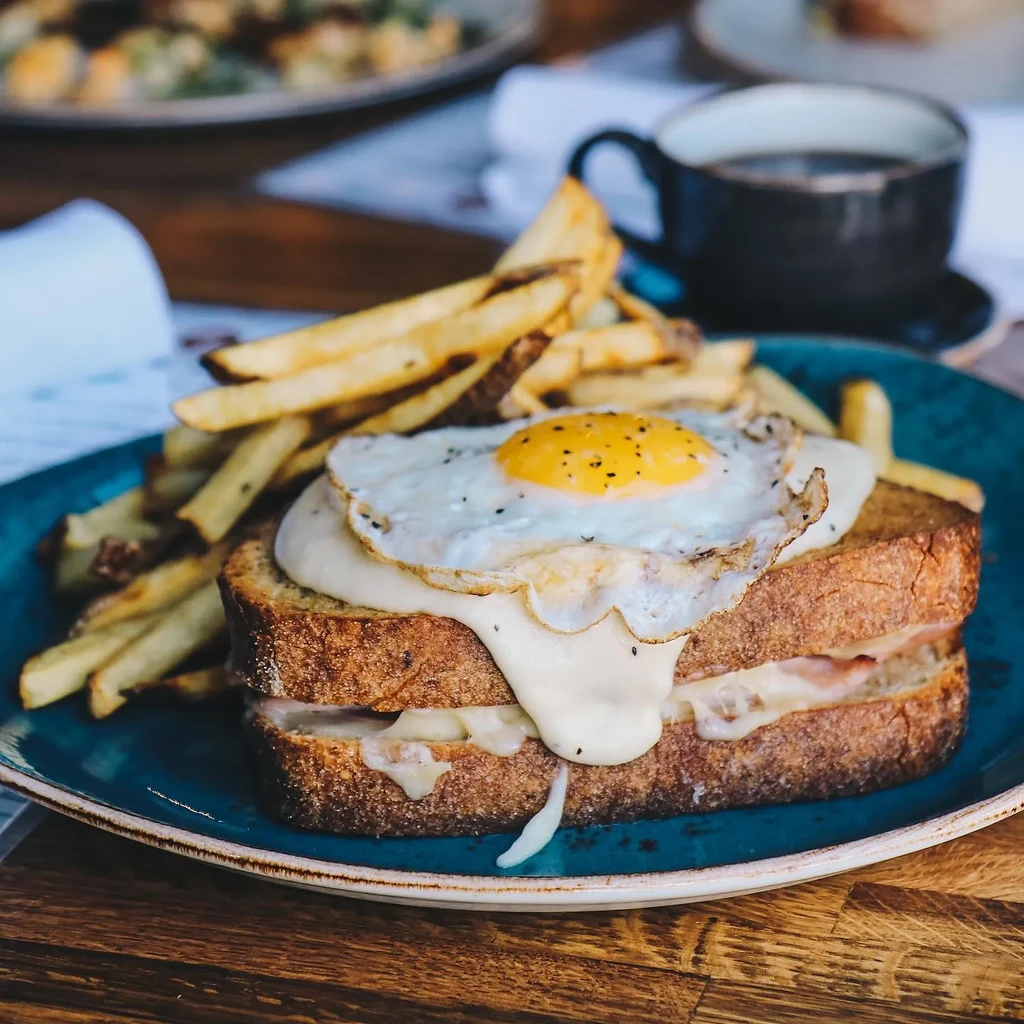 Croque Madame with runny egg and french fries on a teal plate.