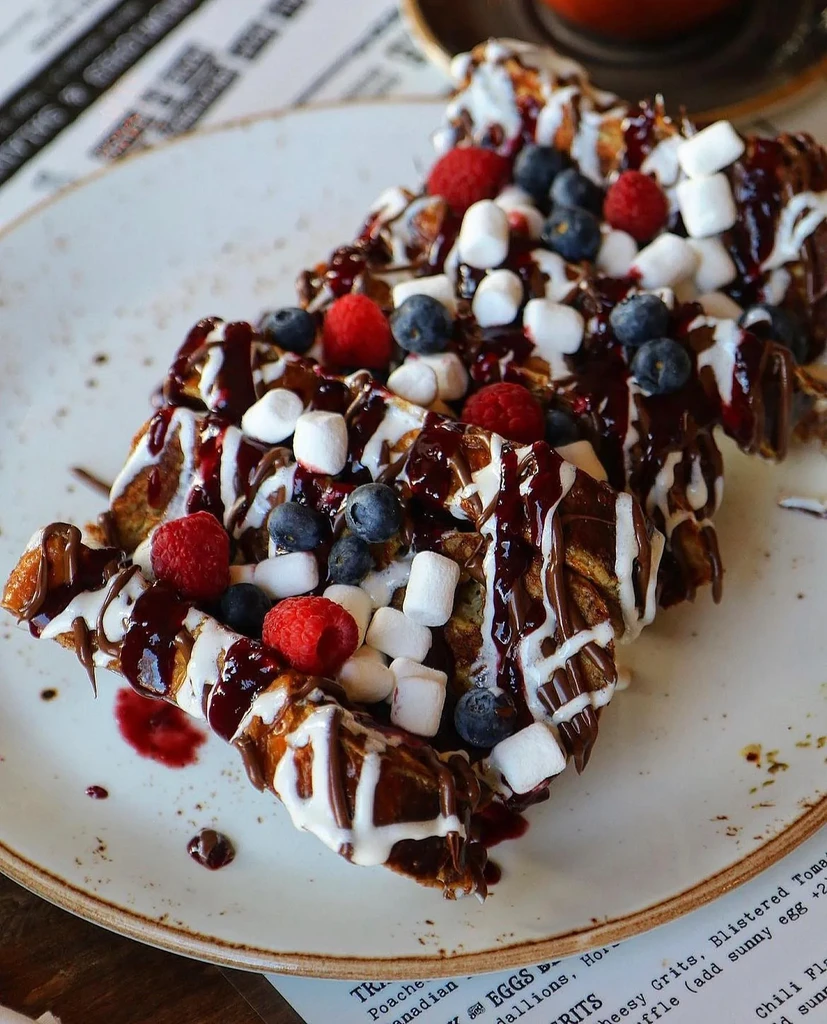 Waffles or French toast generously topped with chocolate, berries, and marshmallows.