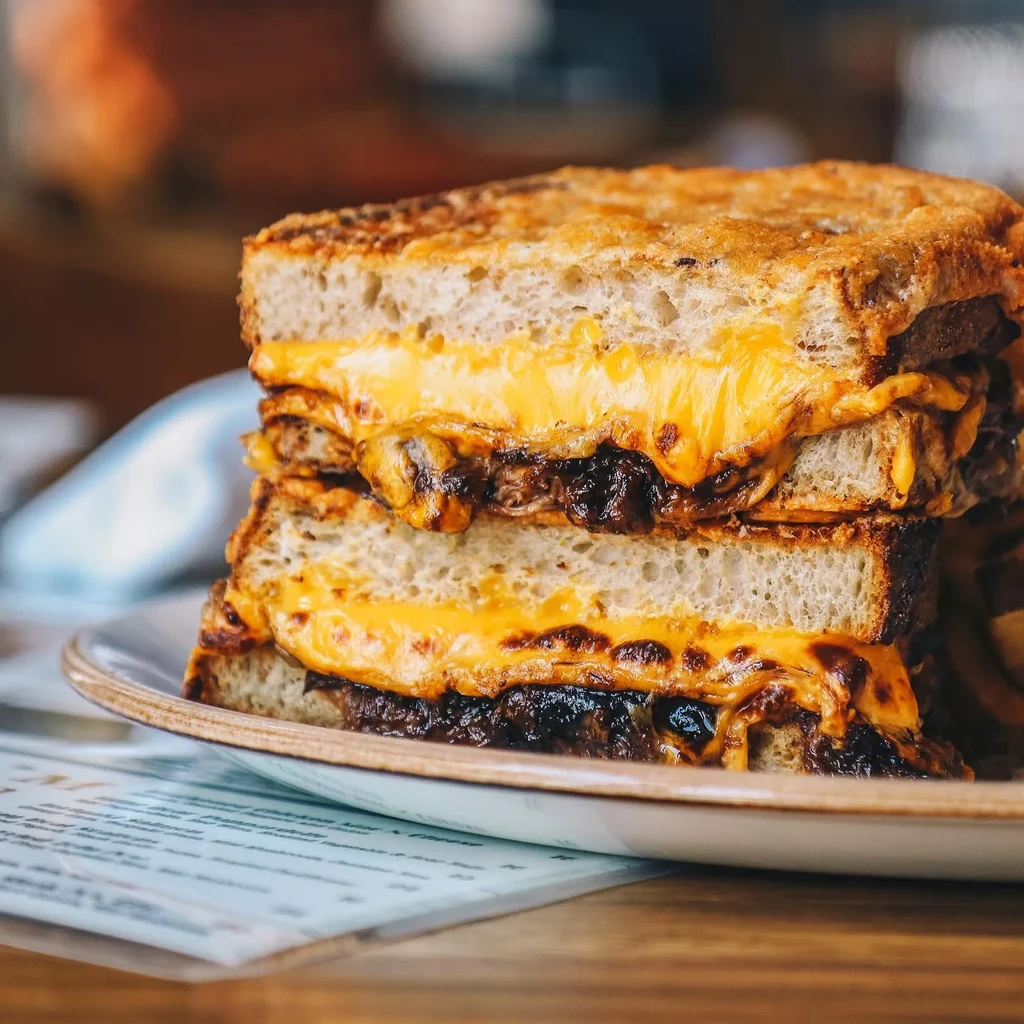 Stacked grilled cheese sandwich with oozing melted cheese and dark filling.