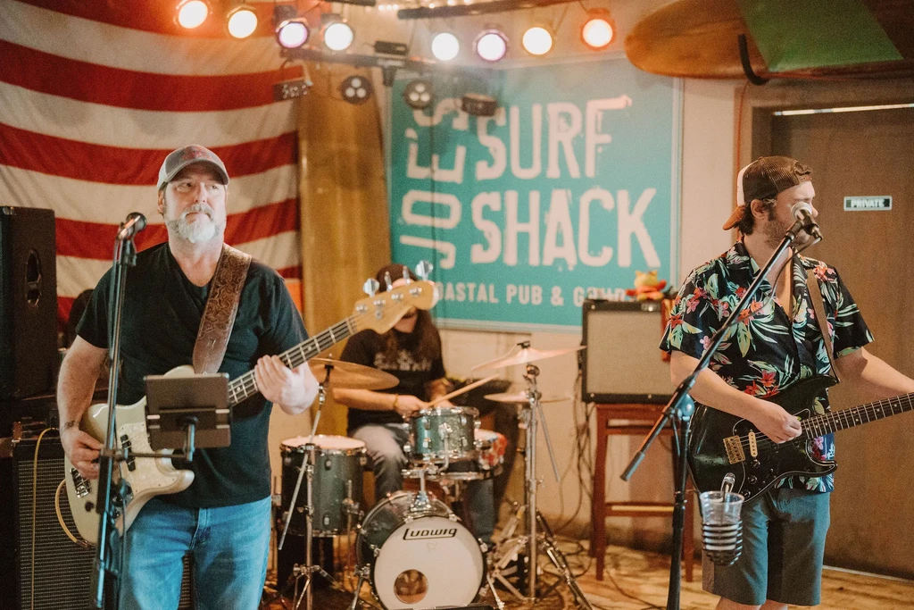 Live band plays bass, guitar, drums at Surf Shack pub.