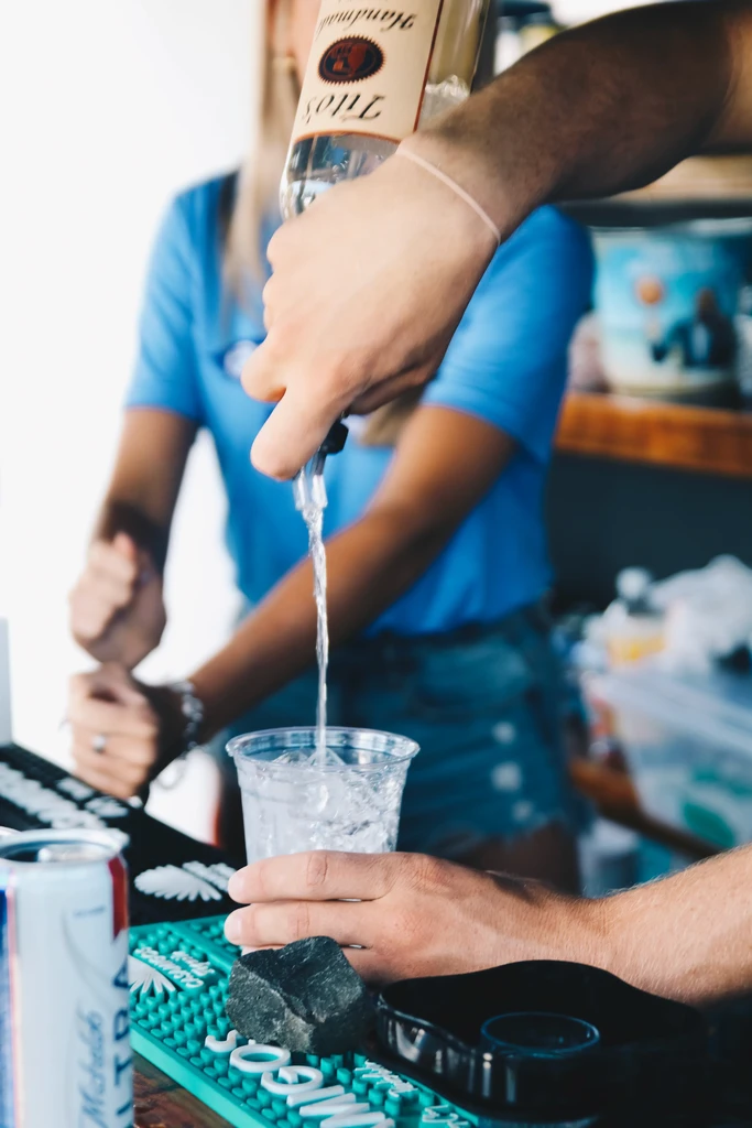 Hands pouring Tito's Vodka into iced cup on Casamigos mat.