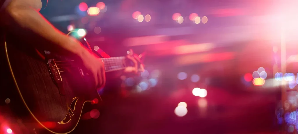 Close-up: Hand playing acoustic guitar, blurred colorful stage lights.