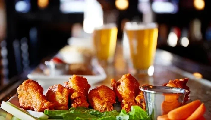 Chicken wings, vegetables, sauce, and two beers on a restaurant table.