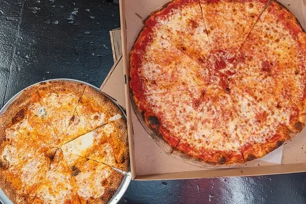 Two New York-style cheese pizzas, one on a pan, one in a box.