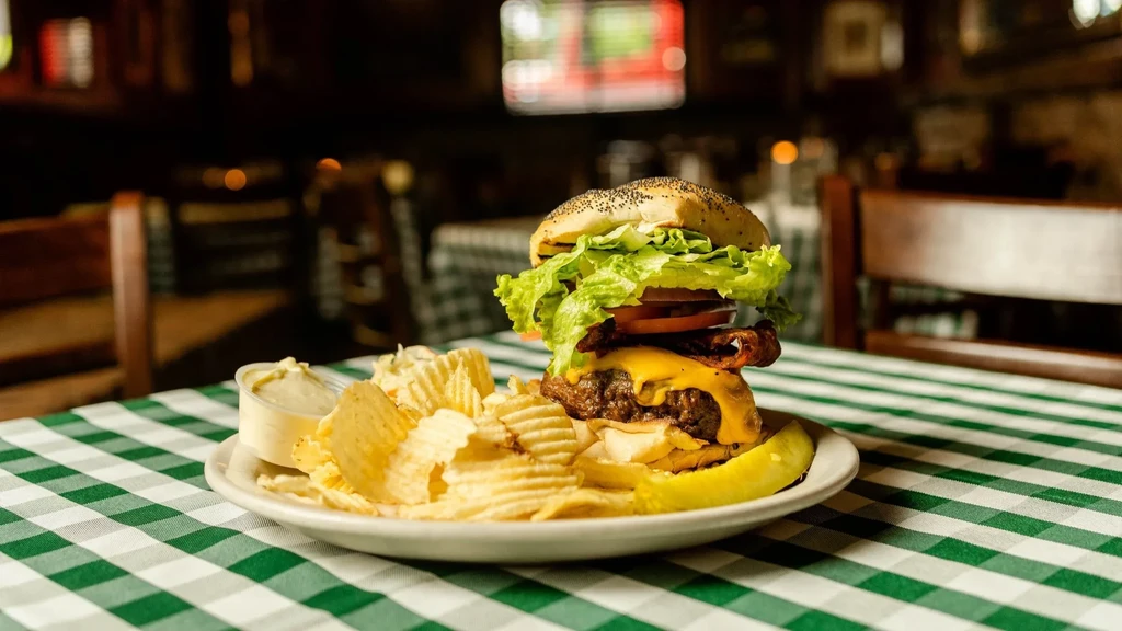 Stacked burger, chips, and pickle on a green checkered tablecloth.