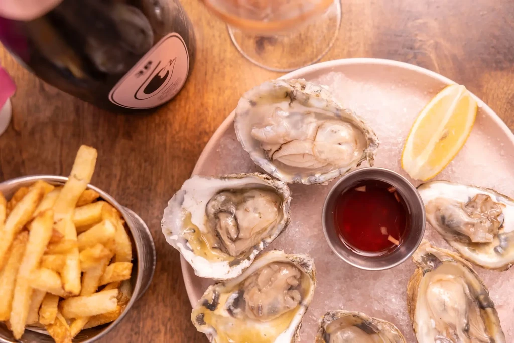 Oysters on ice, french fries, and rosé wine on a wooden table.