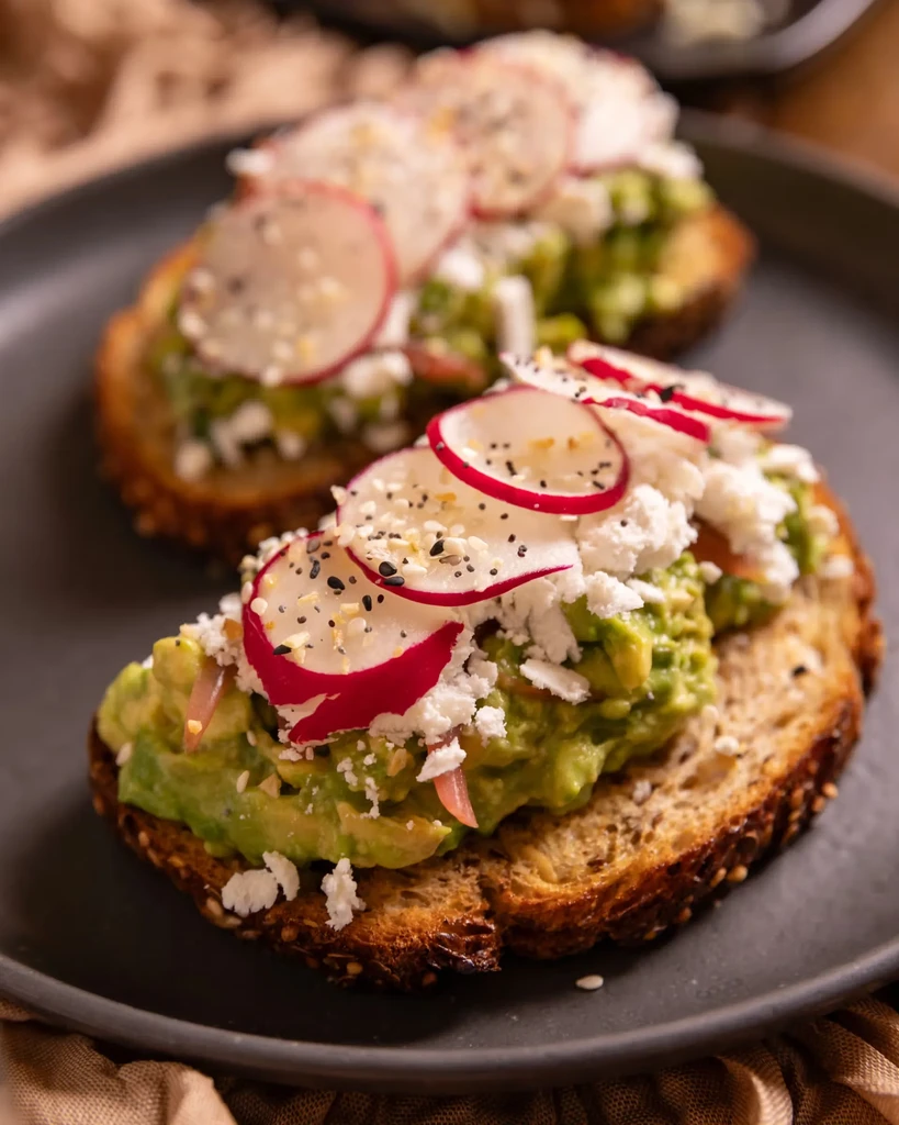 Two rustic avocado toasts with cheese, radishes, everything seasoning.