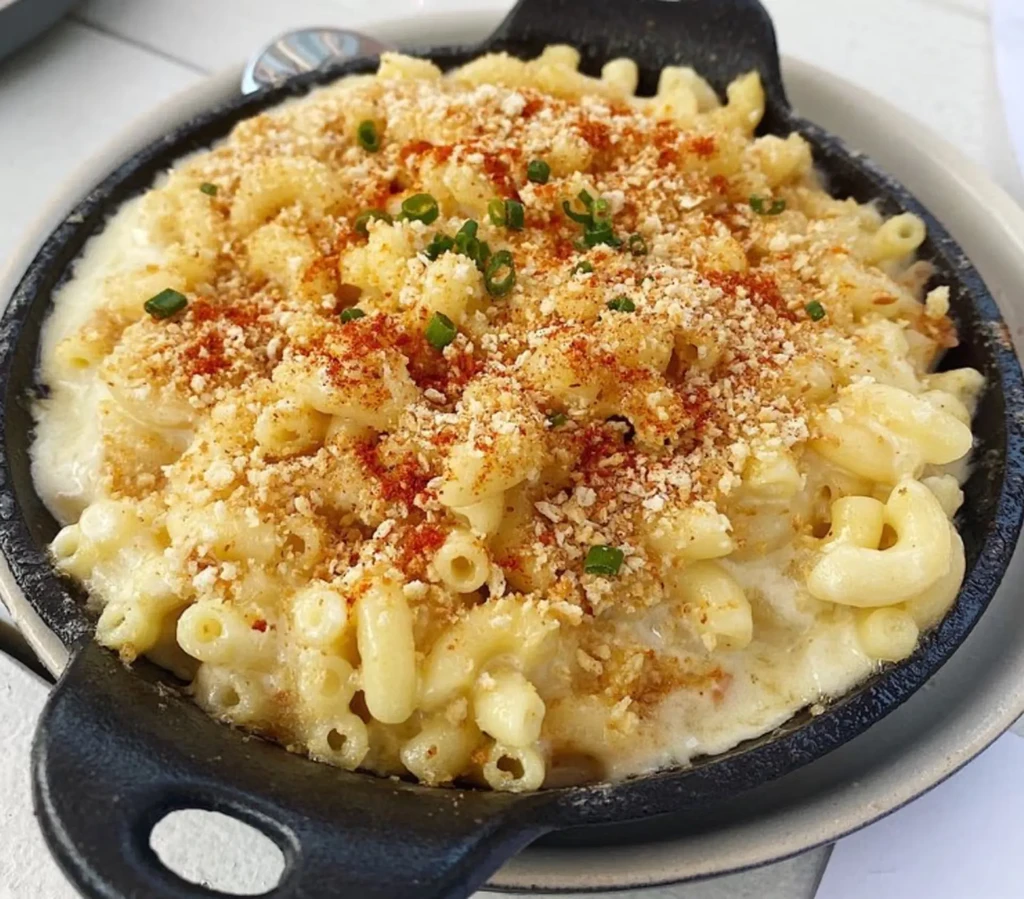 Creamy macaroni and cheese in a skillet with breadcrumbs, paprika, chives.