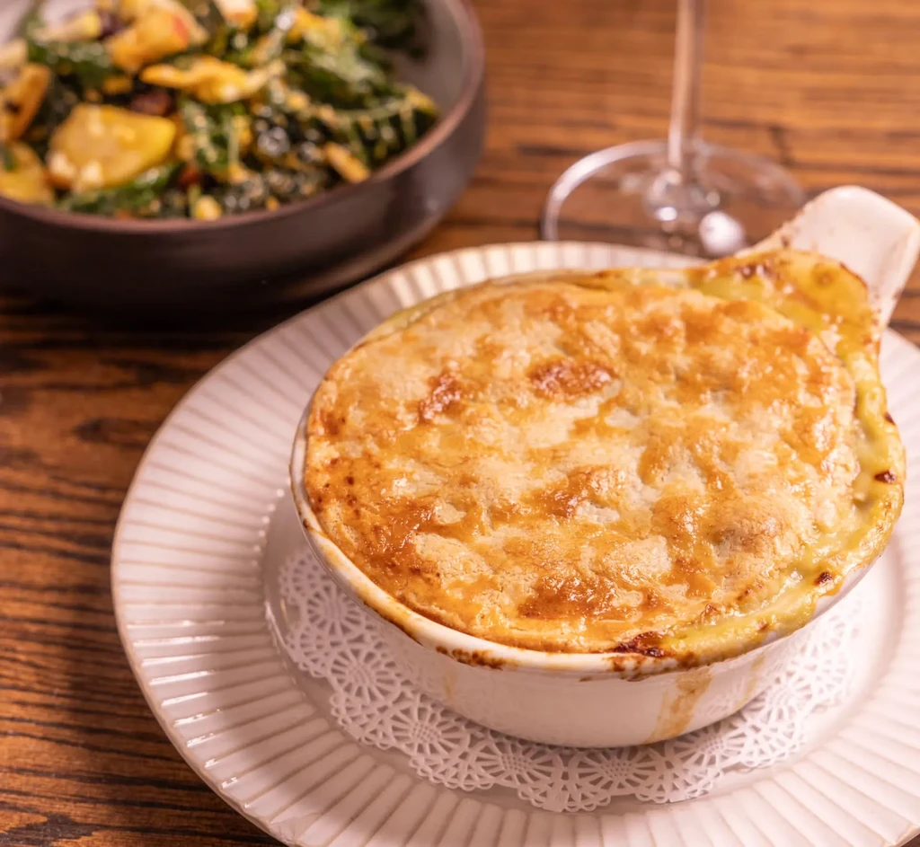 Golden-brown baked pie in a white ramekin, with salad in background.