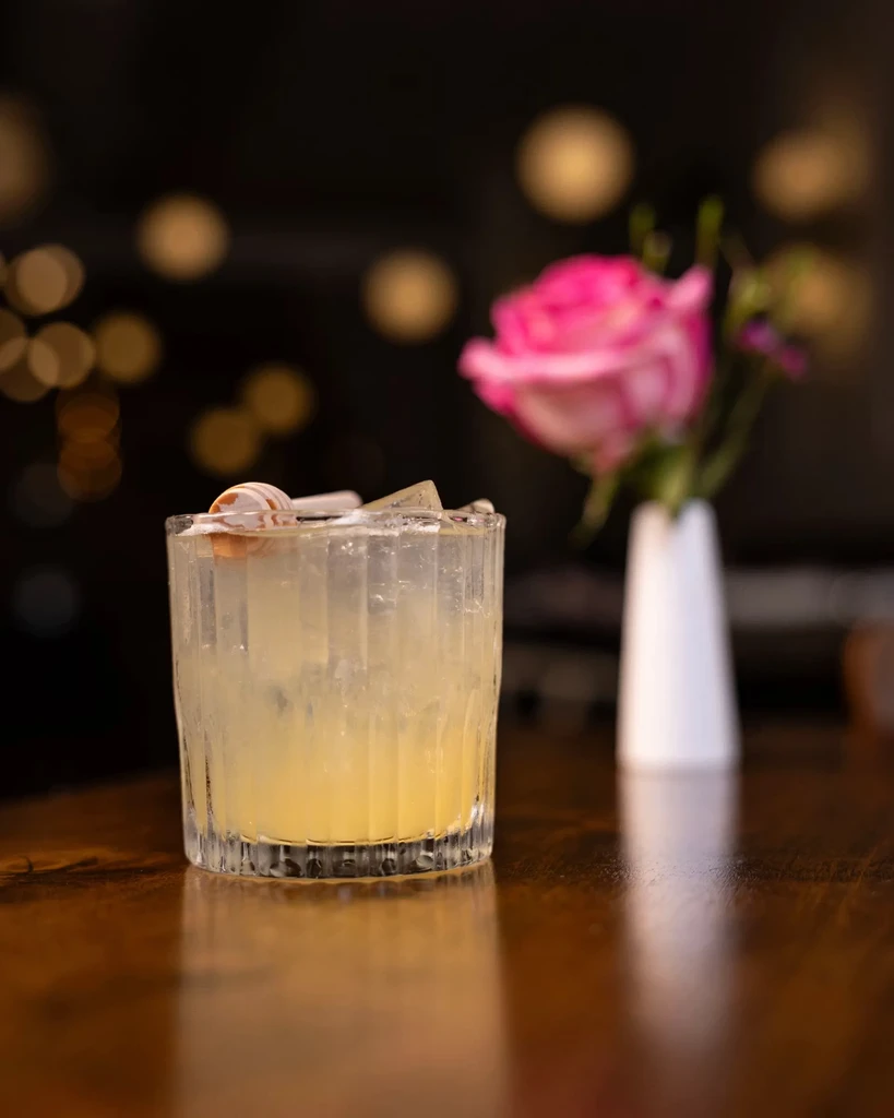 Yellow cocktail in textured glass with ice, honey dipper, and rose.
