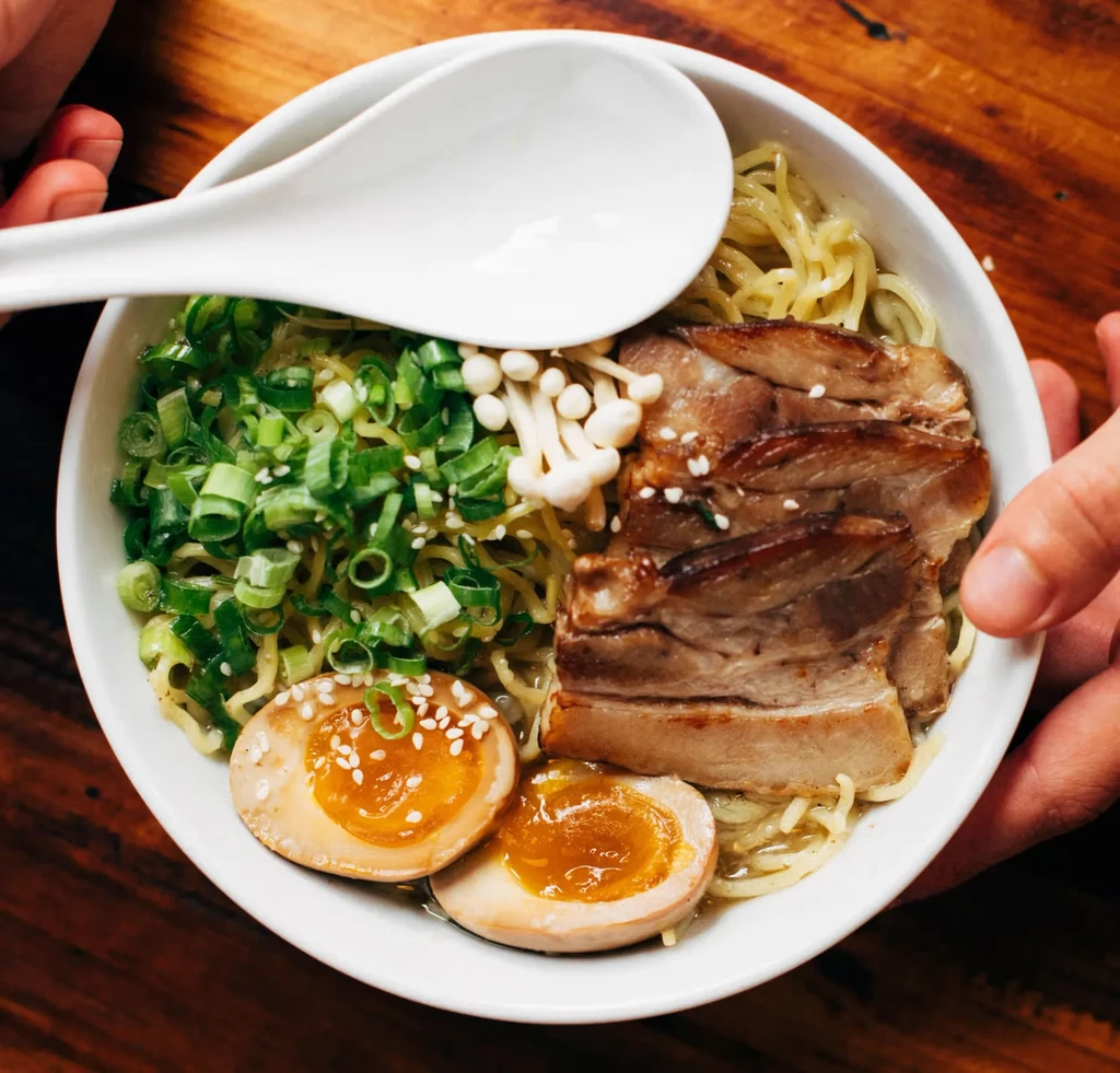 Top-down view of a ramen bowl with pork, egg, scallions, and enoki.