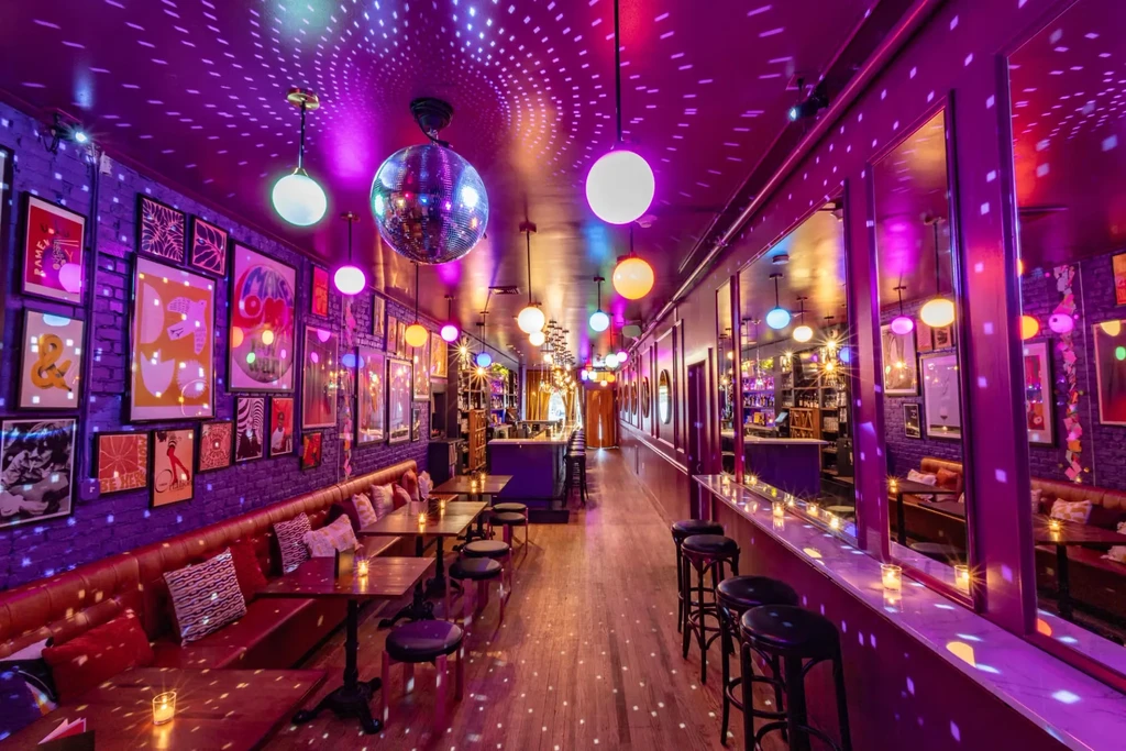 Purple-lit retro bar interior with a disco ball, banquettes, and bar.