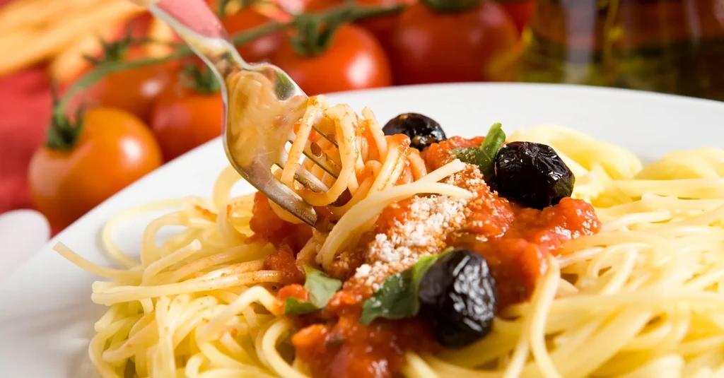 Close-up of a fork twirling spaghetti with tomato sauce, olives, and cheese.
