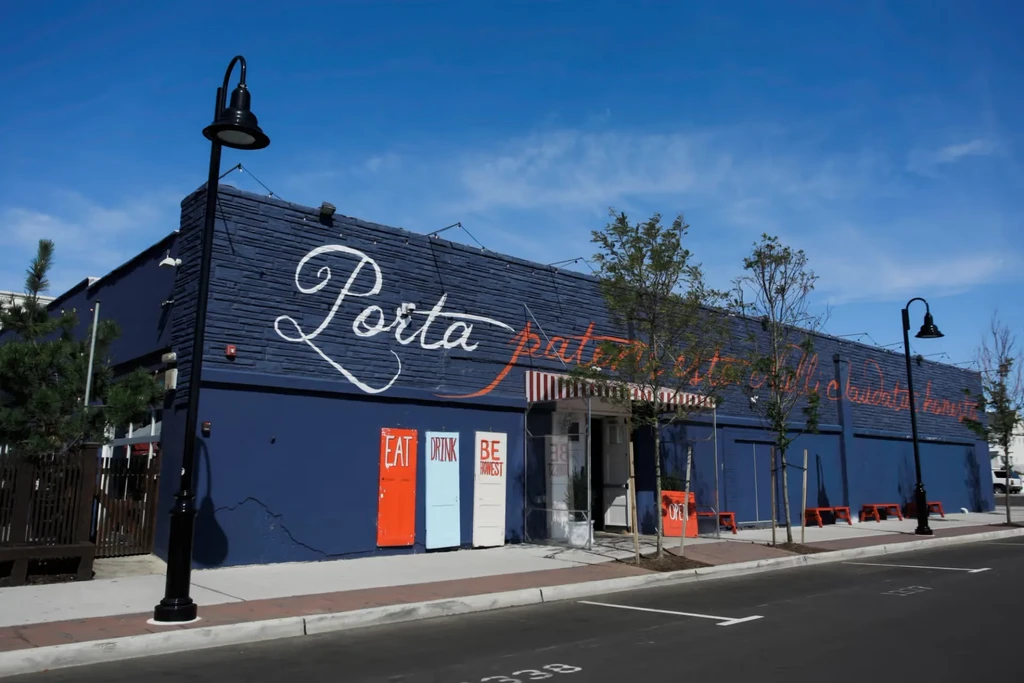 Exterior of deep blue Porta restaurant with "EAT DRINK BE HONEST" signs.