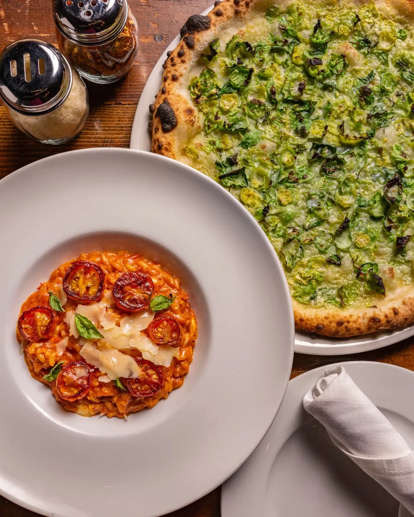 Overhead: Pizza with greens, creamy tomato pasta on a rustic wood table.