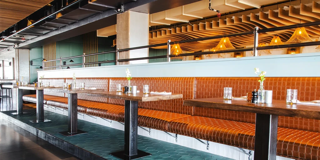 Empty modern restaurant interior with rust-colored booths and wavy wooden ceiling.