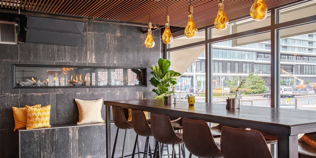 Contemporary restaurant interior with communal table, fireplace, urban view.