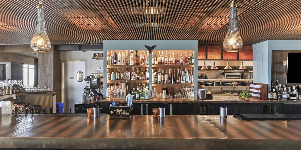 Modern bar with copper counter, whale tail art, and wooden slat ceiling.