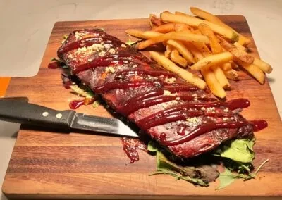Barbecue ribs drizzled with sauce, fries, and knife on a cutting board.