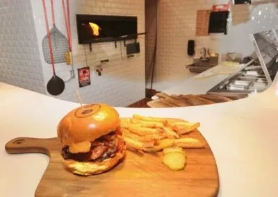 Gourmet burger and fries on wooden board with wood-fired oven.