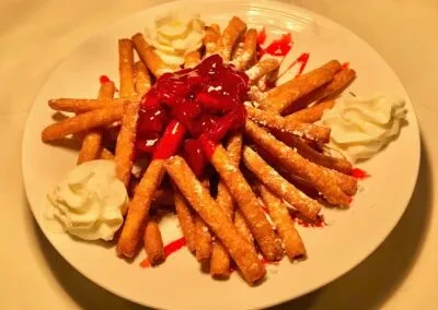 Golden fried dough sticks, red fruit topping, powdered sugar, whipped cream.
