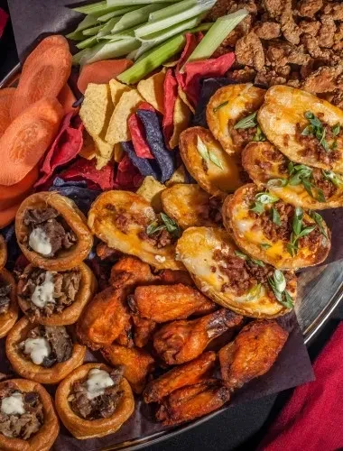 Platter of assorted appetizers: chicken wings, potato skins, vegetable chips.