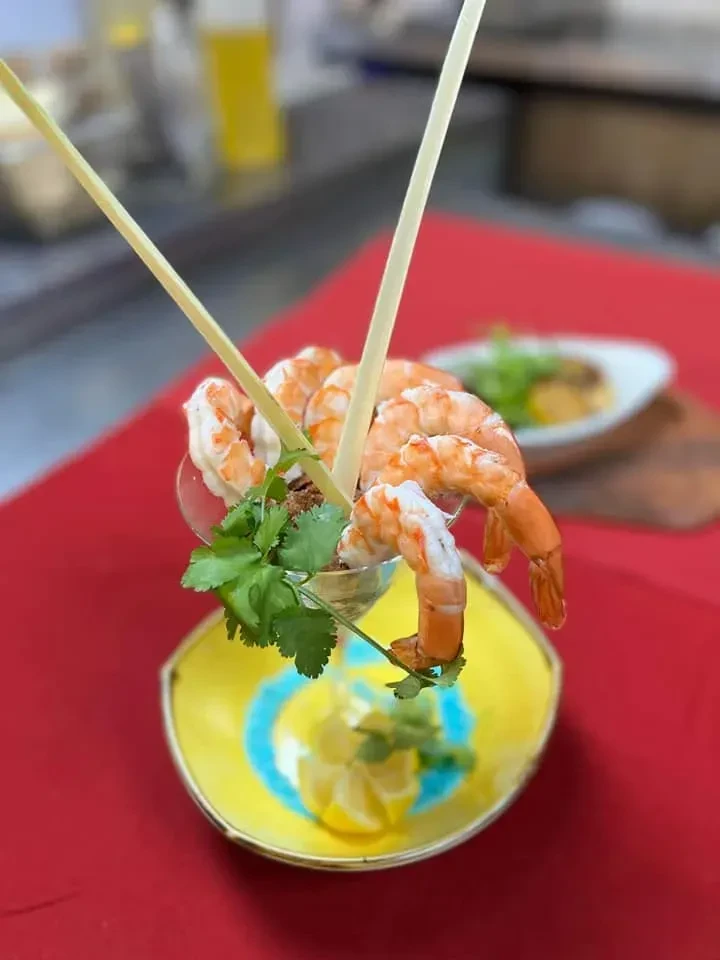Shrimp cocktail with cilantro, lemon, in a glass on a patterned dish.