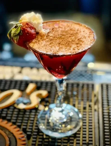Red cocktail in martini glass with strawberry, foam, and powder.