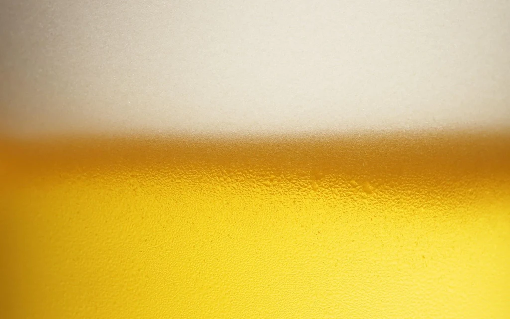 Golden beer in a glass with frothy foam and condensation.