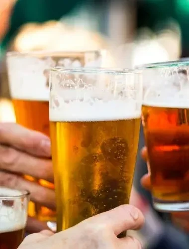 Several hands hold glasses of foamy amber beer in a toast.
