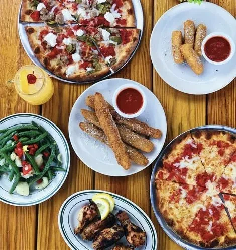 Pizzas, chicken, mozzarella sticks, green beans, and drink on wooden table.