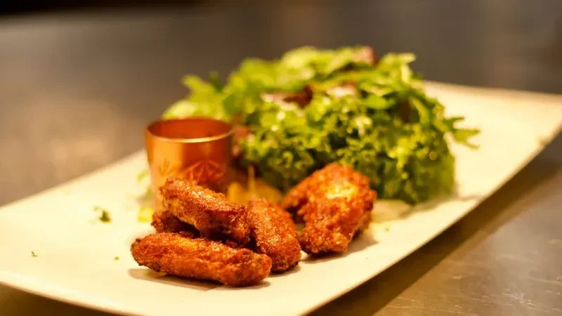 Crispy fried chicken wings, green salad, and dipping sauce on a plate.
