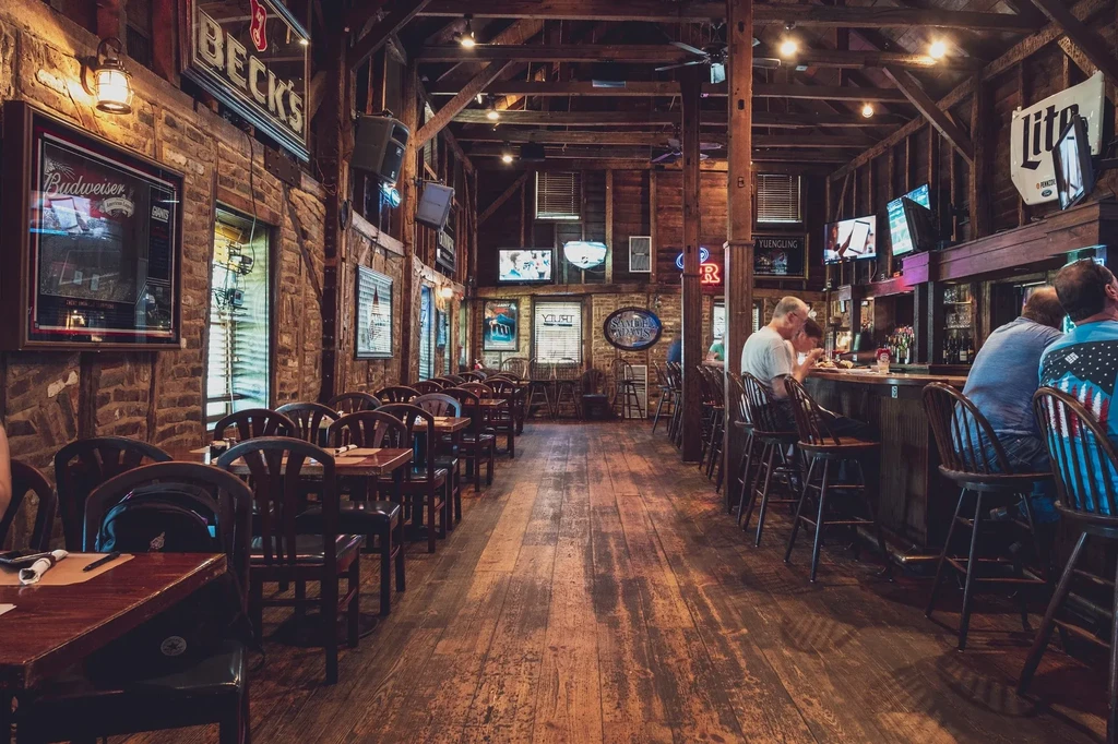 Rustic restaurant and bar interior with patrons, tables, and beer signs.