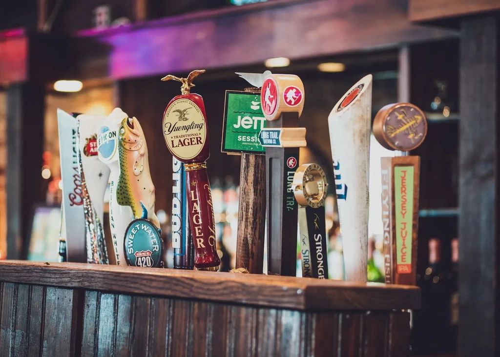 Diverse beer and cider tap handles lined up on a dark bar.