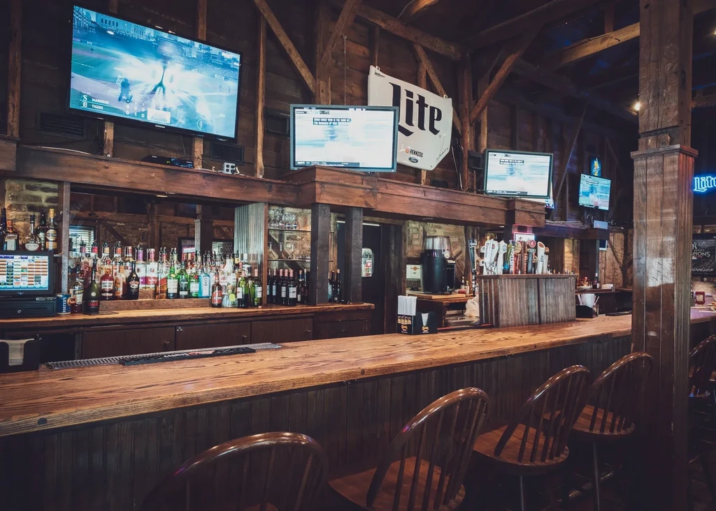 Well-stocked rustic dark wood bar with liquor bottles and sports TVs.