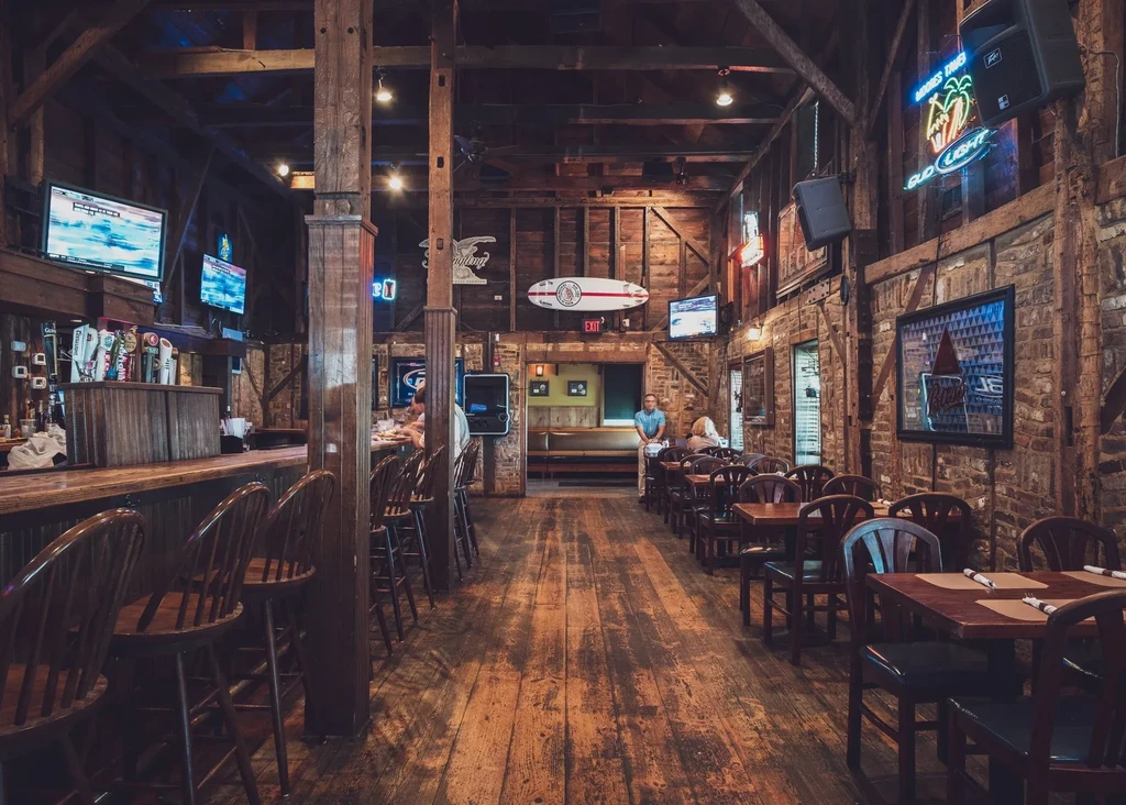 Rustic barn-style restaurant interior with wooden bar, dining tables, and patrons.