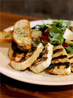 Plate with grilled halloumi slices, garlic bread, and fresh green salad.