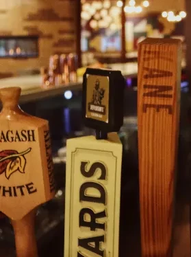 Three blurred beer tap handles, labeled Allagash White, Ards, Lane.