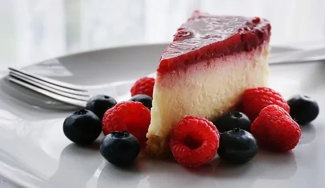 Slice of cheesecake with red berry glaze, blueberries, and raspberries.