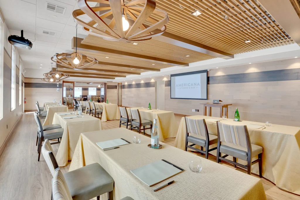 Empty, well-lit conference room with tables and "AMERICANA KITCHEN & BAR" screen.