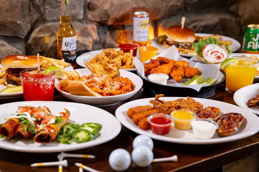 A wooden table full of fried food, drinks, and golf accessories.