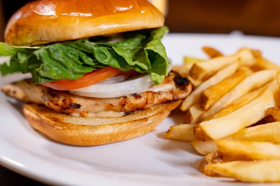 Grilled chicken sandwich and crispy fries on a white plate.