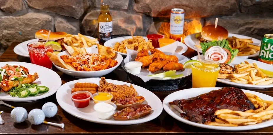 Rustic table piled with fried food, cocktails, beer, and golf balls.