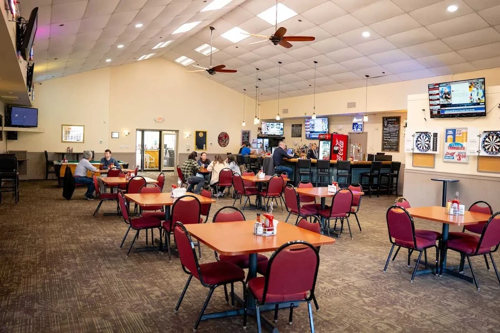 Casual restaurant and bar interior with tables, bar, TVs, and dartboards.