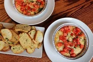 Two ramekin appetizers, crostini, tomatoes, and herbs on a wooden table.