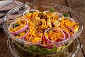 Green salad with cheese, croutons, and onion in a plastic bowl.
